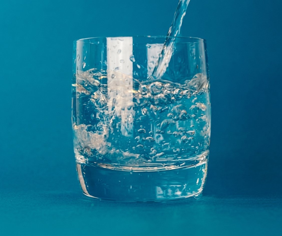Water pours into a clear glass against a blue background.