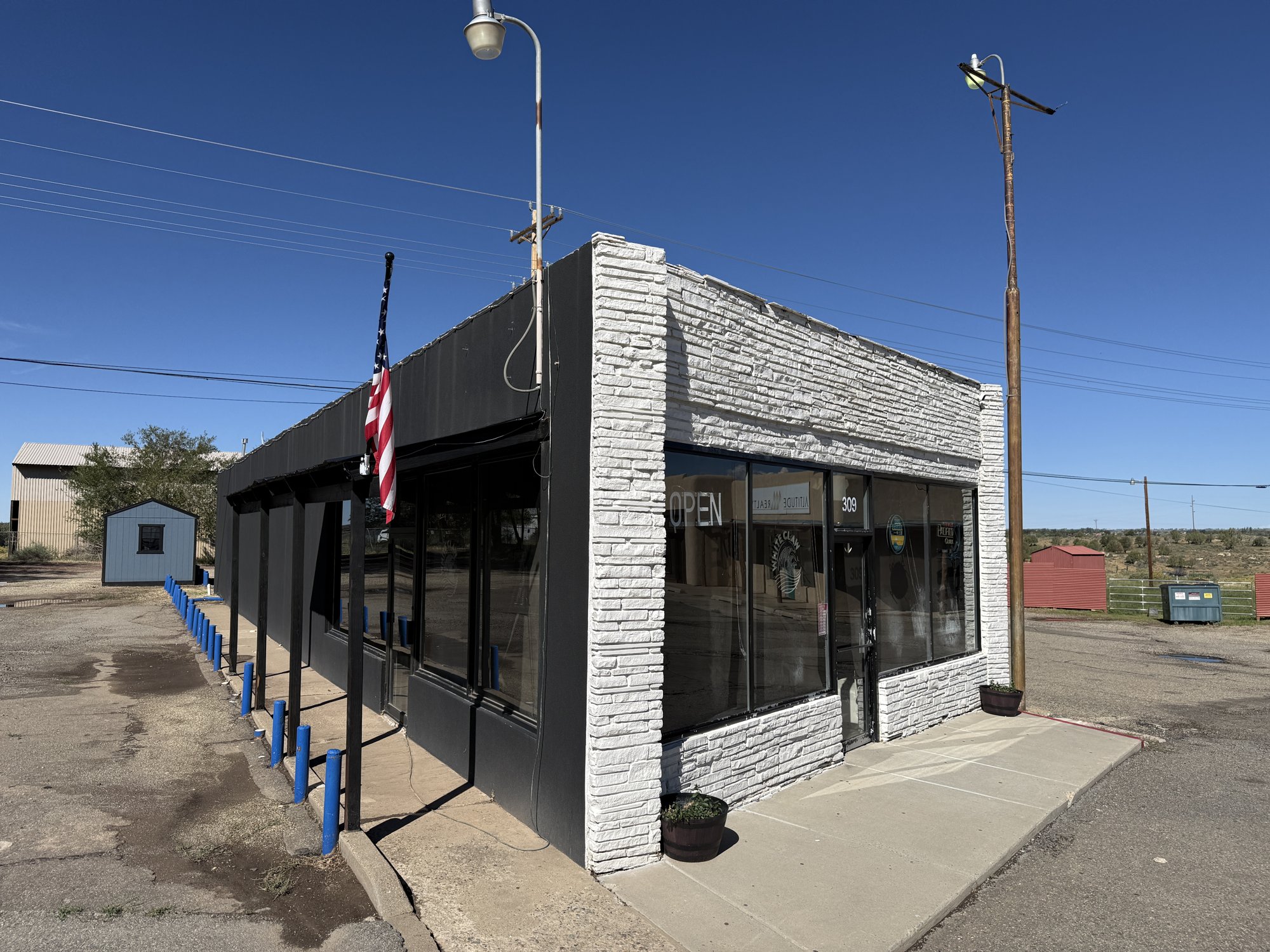 A one-story building with a white stone front, black siding and large windows at 309 N. Broadway in Cortez, with an Open sign in the window, an American flag and blue posts along the side.